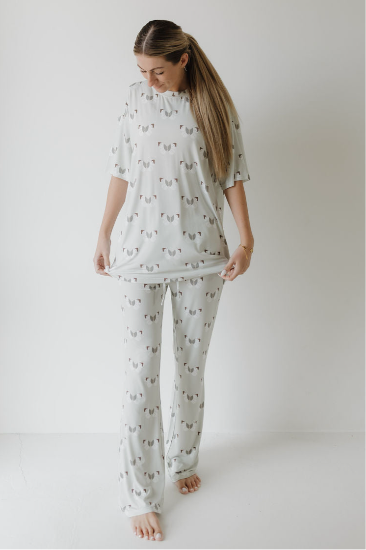 A woman stands barefoot in a white room, wearing the forever french baby Short Sleeve Women's Bamboo Pajamas in the Butterflies print. She looks down and holds out the hem of her hypo-allergenic sleepwear top with both hands.