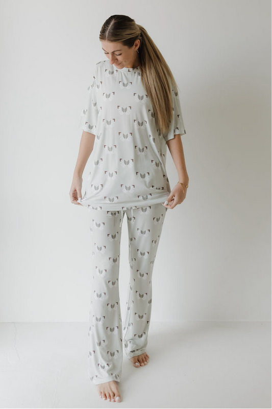 A woman stands barefoot in a white room, wearing the forever french baby Short Sleeve Women's Bamboo Pajamas in the Butterflies print. She looks down and holds out the hem of her hypo-allergenic sleepwear top with both hands.