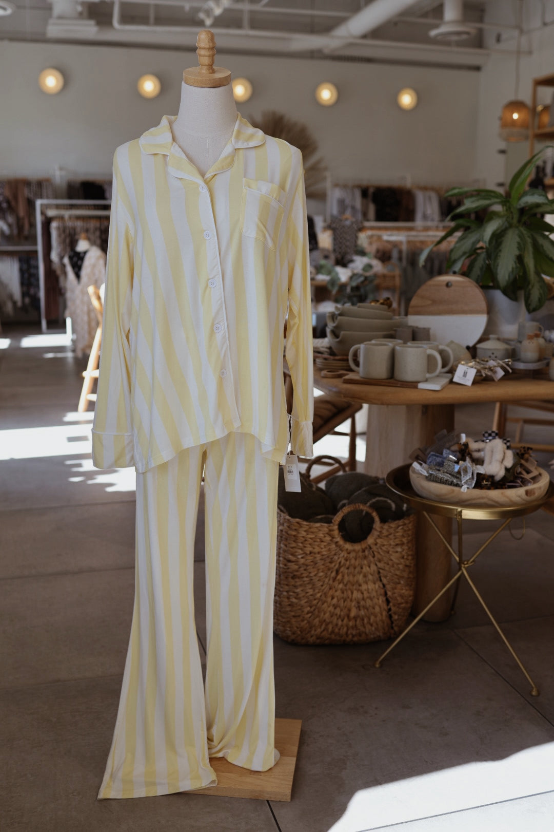 A mannequin showcases the forever french baby Long Sleeve Women's Bamboo Pajama in Butter—a yellow and white striped set—inside a well-lit boutique surrounded by home goods and decor.