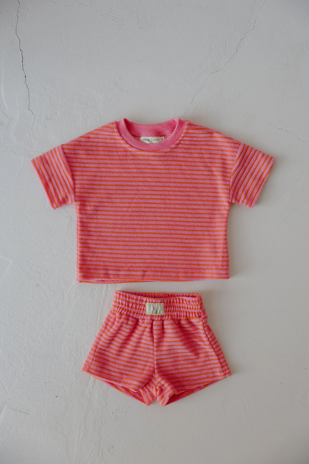 The forever french baby Child Terry Short Set | Strawberry features a pink and orange striped short-sleeve top with elastic-waist shorts, displayed flat on a light textured surface—ideal for family moments.