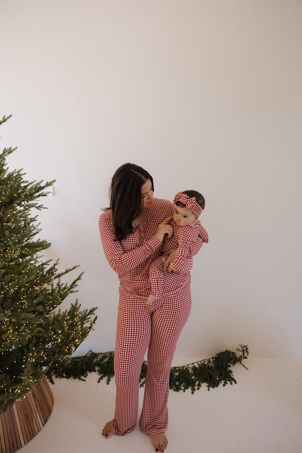 A woman and baby wear forever french baby matching hypoallergenic Women's Bamboo Pajamas in Red Gingham, posing together beside a decorated Christmas tree against a plain white background.