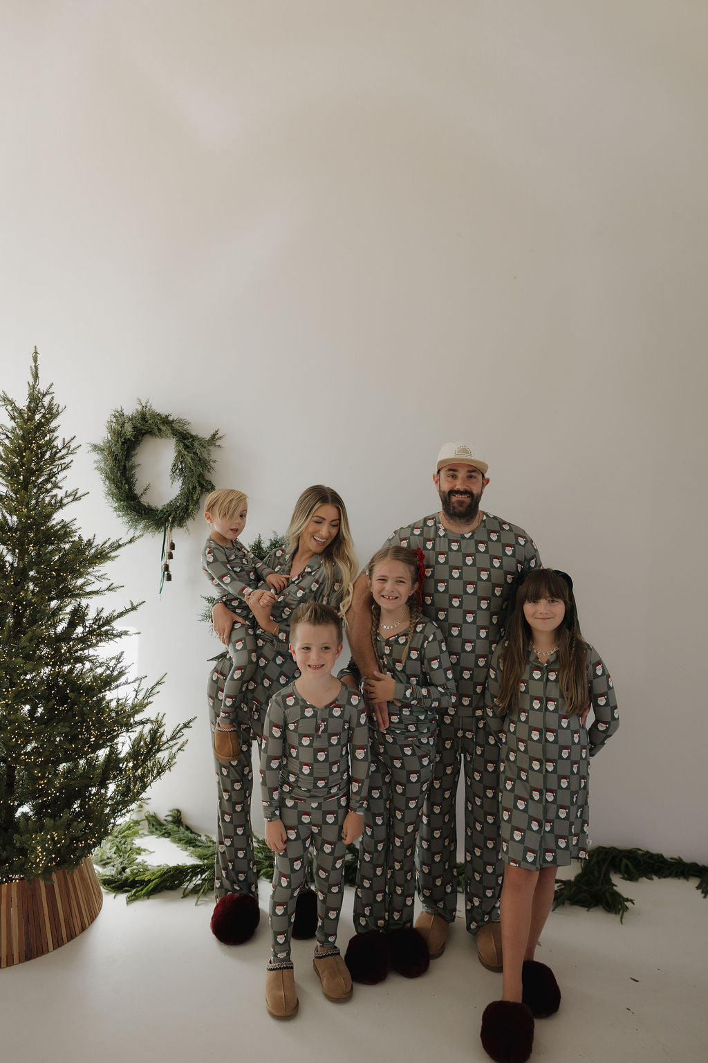 A family of six in matching gray holiday pajamas smiles by a tree and wreath—captured for Santa Photos | Forever French Baby x Emily Schuman Photography, Gilbert AZ, by Emily Schuman Photography.