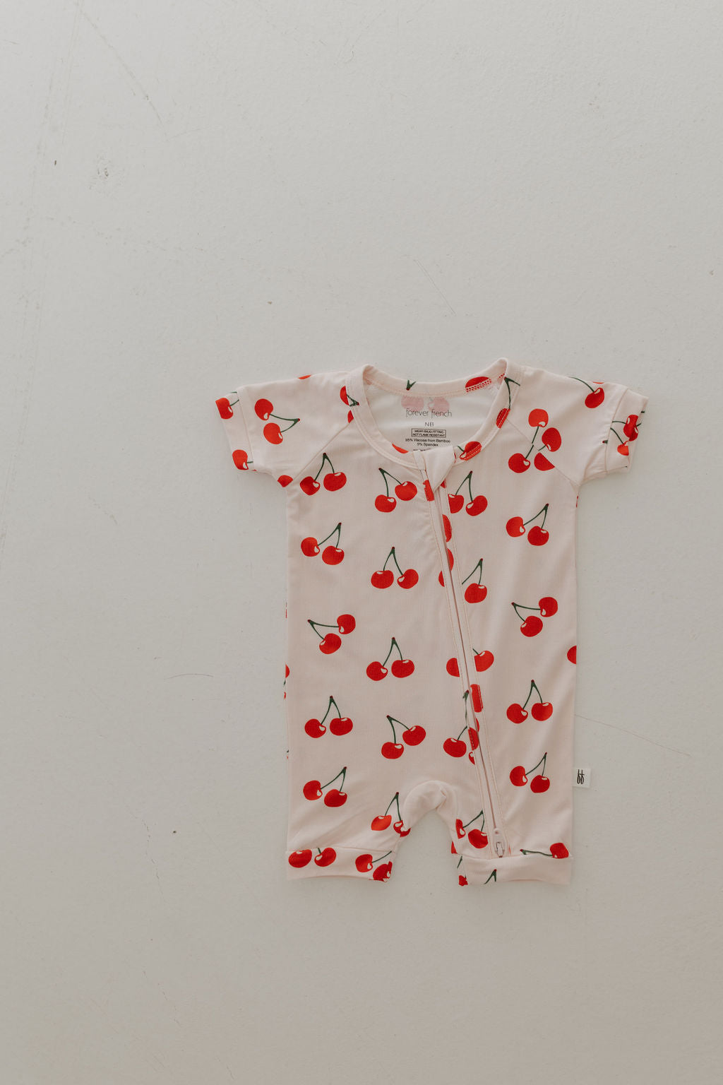 The Bamboo Zip Shortie by forever french baby features a charming cherry pattern on breathable bamboo fabric, complete with a front zipper, laid flat on a light background.