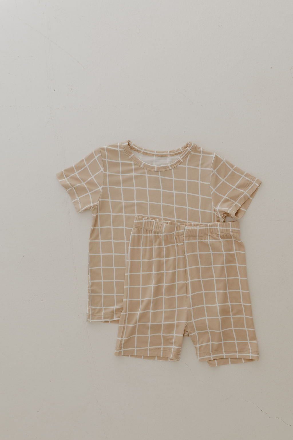 The Bamboo Short Set | Grid by forever french baby features a beige short-sleeve shirt and shorts with a white grid pattern, crafted from breathable fabric, displayed on a light surface.