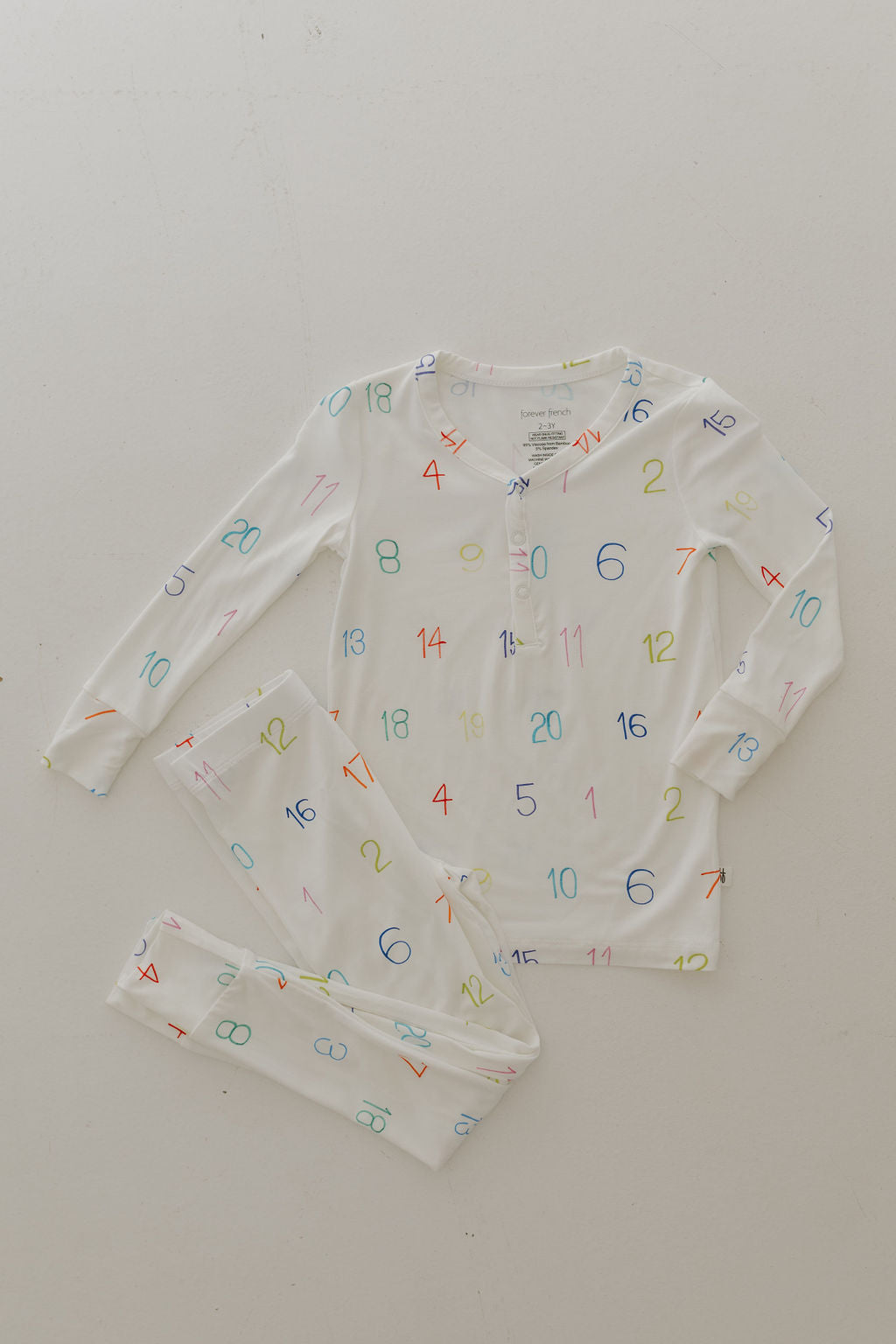 The Bamboo Two Piece Pajamas | Charli Counts by forever french baby offers hypo-allergenic comfort with a white long-sleeve top and pants featuring colorful numbers in red, blue, green, and yellow. This playful design promotes autism awareness while catering to sensitive skin.