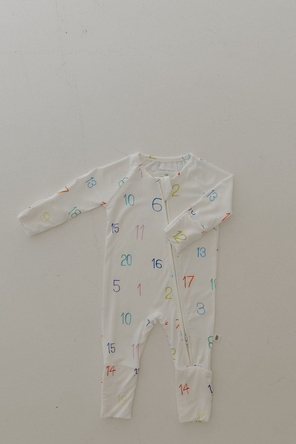 The Bamboo Zip Pajamas | Charli Counts by forever french baby is a white long-sleeve baby onesie featuring multicolored numbers. Crafted from hypo-allergenic bamboo fabric, it has a diagonal zipper from the neckline to the left foot, set against a light-colored background for a gentle design.