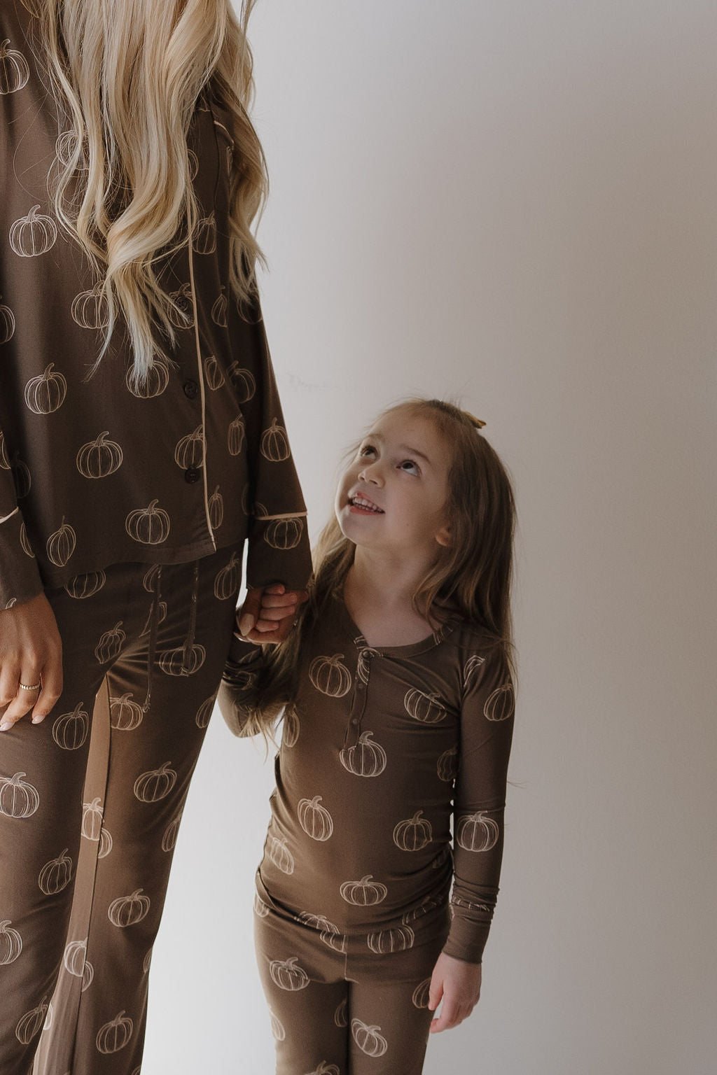 A young girl and an adult, both in forever french baby loungewear—including the Women's Bamboo Button Up Lounge Set in Brown Pumpkin—stand together against a light backdrop, highlighting cozy, hypo-allergenic family pajamas.