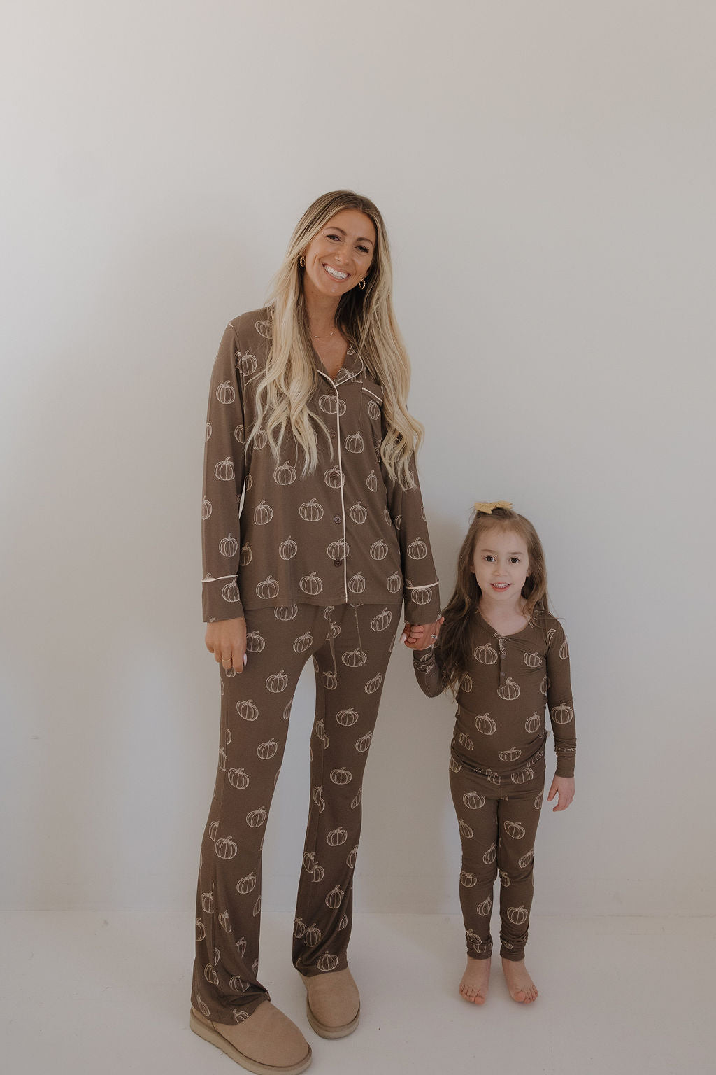 A woman and young girl smile and hold hands, wearing matching forever french baby Bamboo Two Piece Pajamas | Brown Pumpkin—cozy, breathable bamboo sleepwear for all ages. The girl is barefoot; the woman wears slippers.