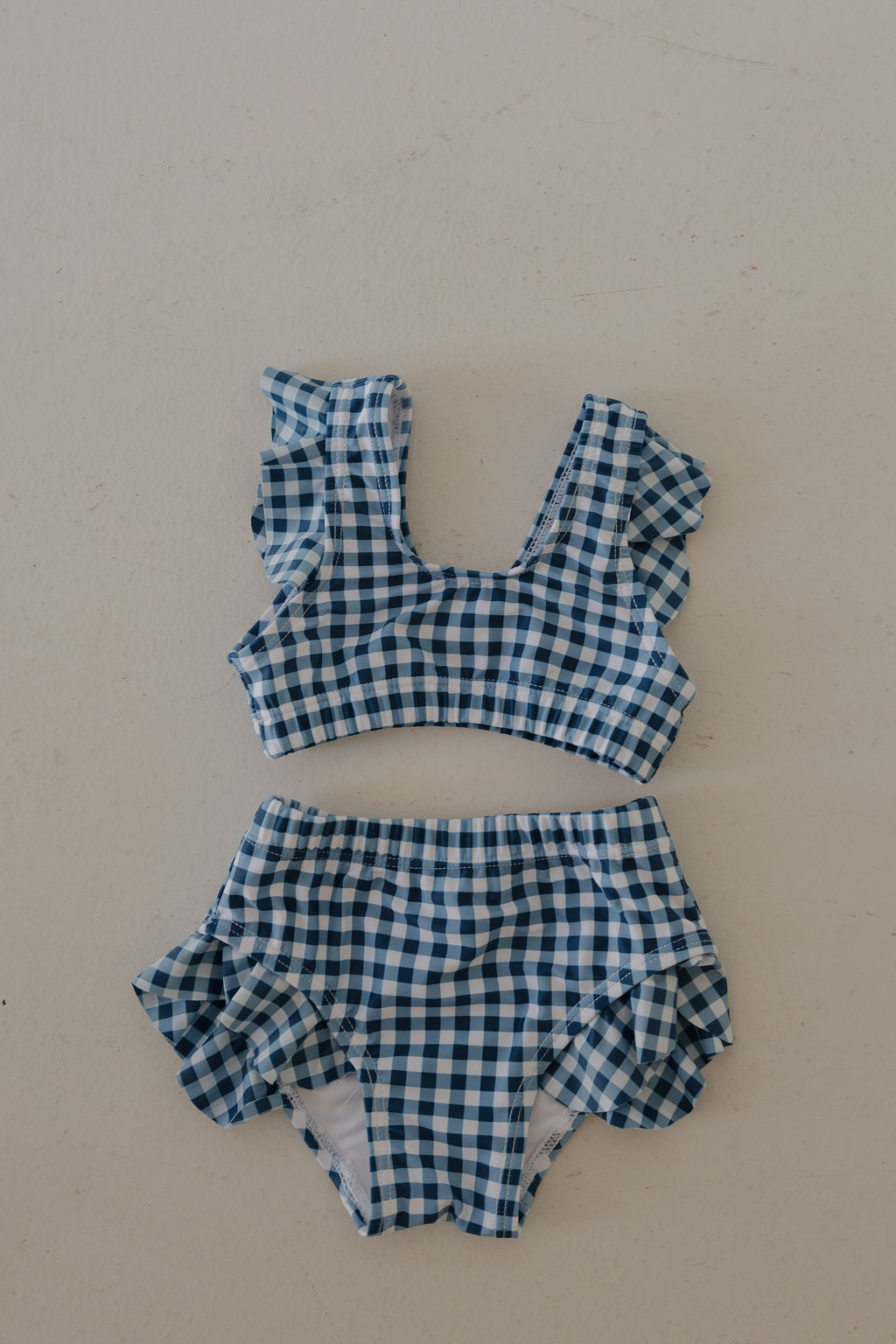 The forever french baby Girls Two Piece Swimsuit in blue gingham features ruffled shoulder straps and ruffled leg openings on high-waisted bottoms, shown flat on a light background.