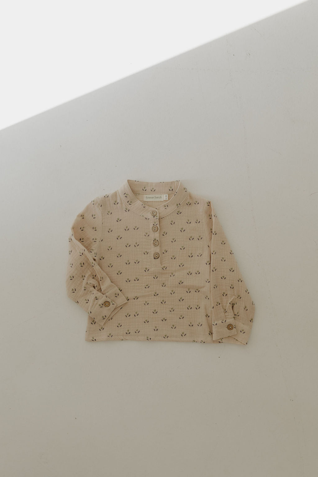 The Muslin Button Up | Flora by forever french baby is a light beige, floral-patterned, long-sleeve muslin cotton shirt with buttoned cuffs and a short button placket—an ideal addition to any kids' clothing collection.