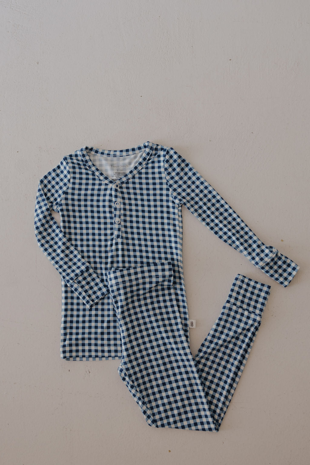 The forever french baby Bamboo Two Piece Pajamas in Blue Gingham are hypoallergenic kids' sleepwear, featuring a breathable long-sleeve button-up top and matching pants, shown laid flat on a light background.
