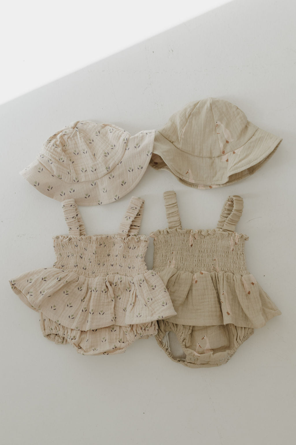 Two beige Sleeveless Muslin Romper & Hat sets by forever french baby, each with ruffle details, bloomers, and shoulder straps, are paired with matching 100% cotton sun hats and displayed on a white background.