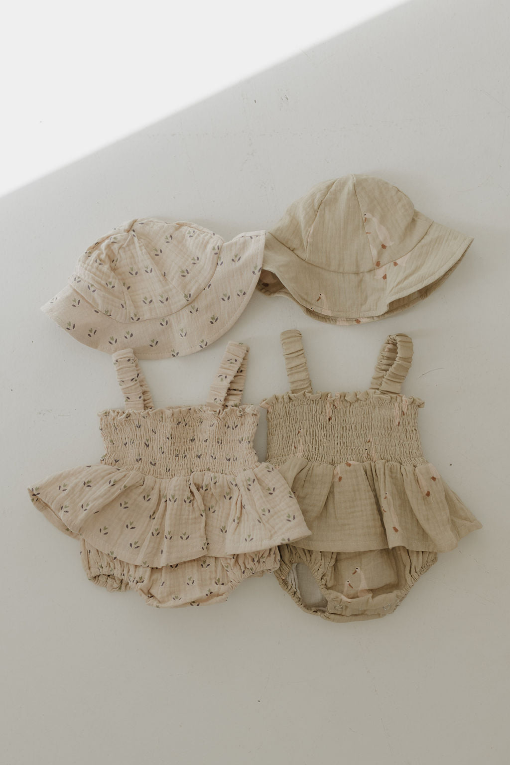 Two sets of Sleeveless Muslin Romper & Hat by forever french baby in light beige: one plain, one with a floral print. Each set has a ruffled cotton romper and matching sun hat, made from 100% cotton and displayed on a white surface.