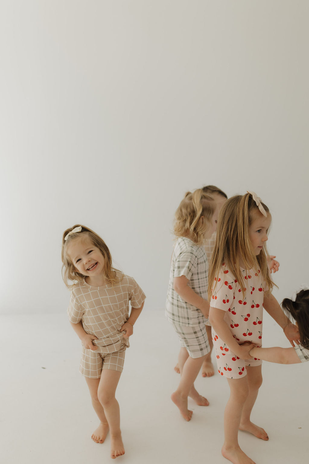 Four young children in playful, cozy outfits enjoy a bright, minimalistic space. One smiles at the camera while others turn away, all dressed in breathable Bamboo Short Sets | Grid by forever french baby—perfect for their endless adventures with checks and cherries.