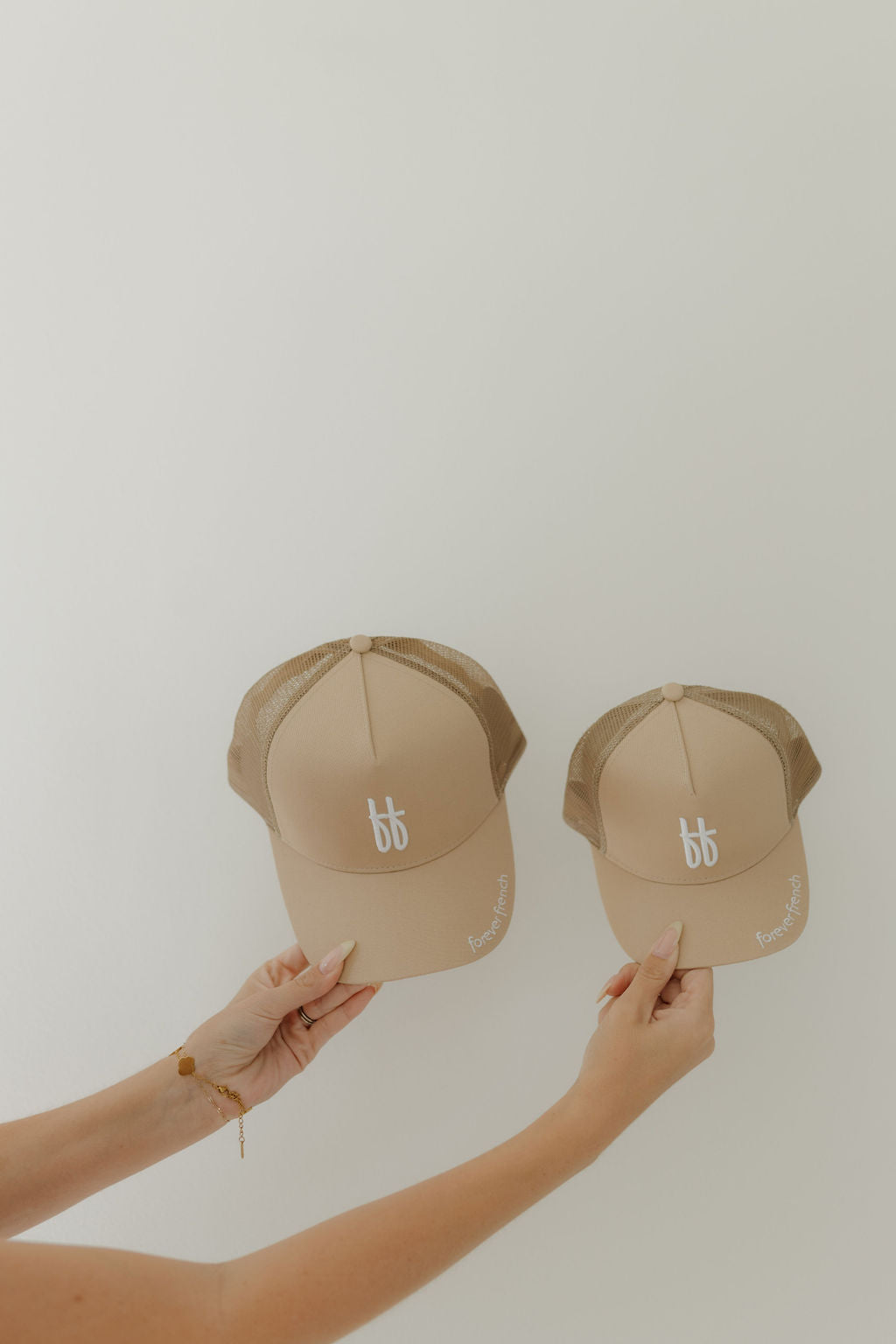 Two ff Tan Children's Trucker Hats from Forever French Baby are displayed against a light backdrop, highlighting their distinctive style. Each features a white "bb" logo and a "Flower Power" brim, exuding elegance.