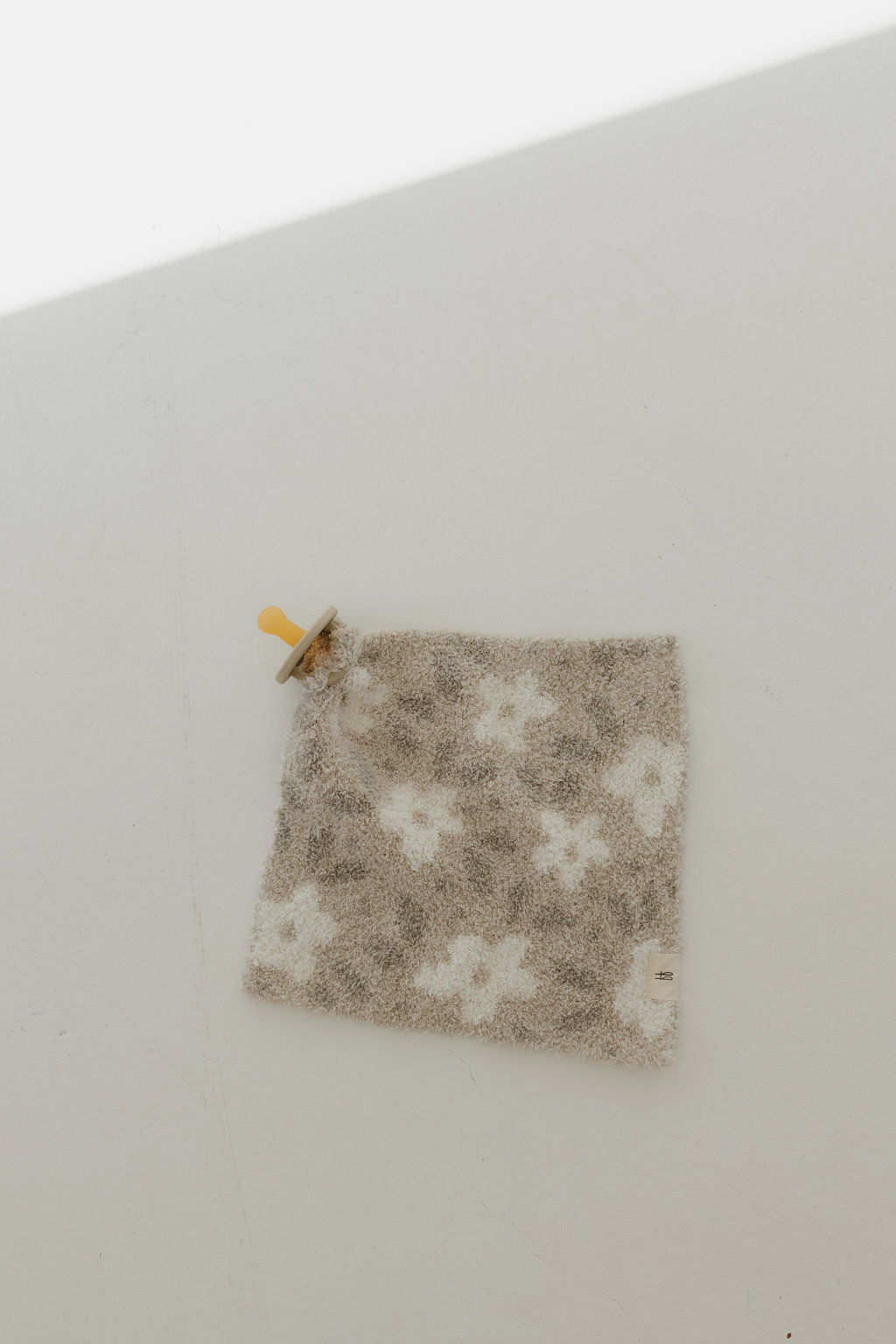 The Forever French Baby Lovey in a French Gray Floral print is displayed flat on a light surface. It features a wooden ring in one corner, potentially serving as a teether or grip, with soft shadows enhancing its elegance.