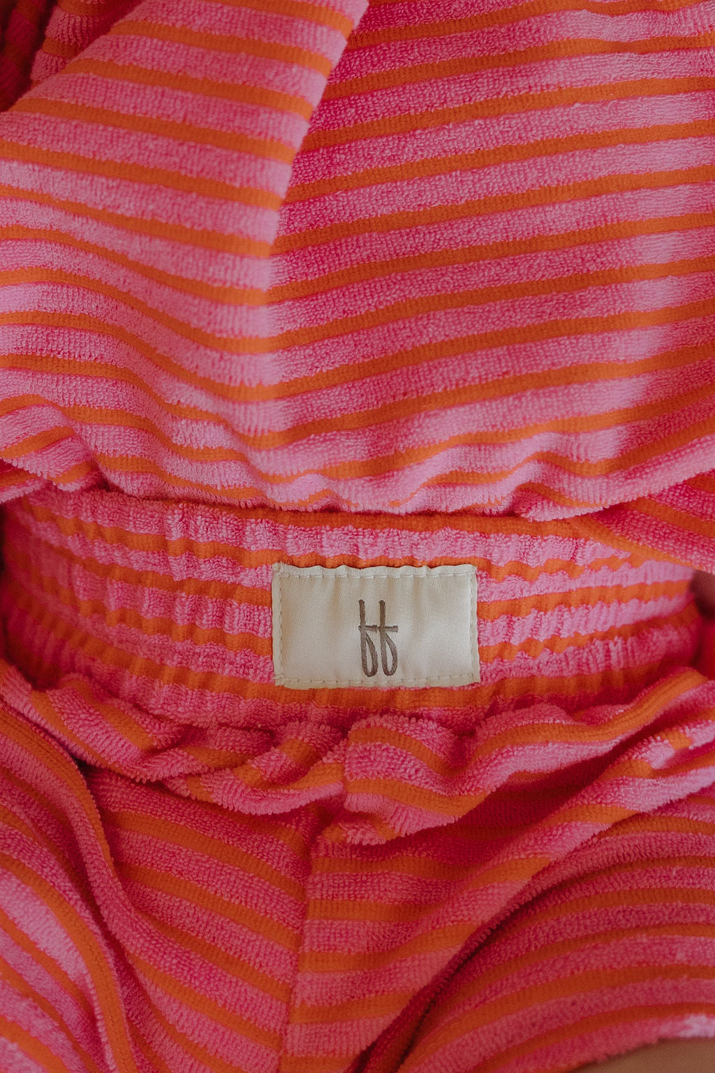 Close-up of the forever french baby Child Terry Short Set in Strawberry, featuring a fabric label with "ff" on pink and orange stripes, elastic waistband, and overlapping layers—perfect for comfy family moments.