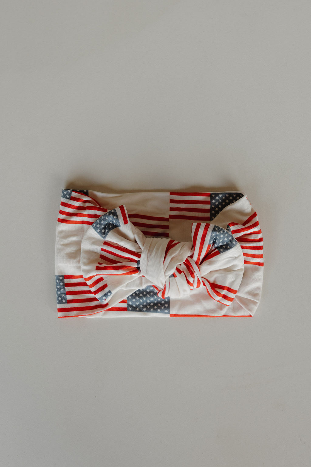The forever french baby Bamboo Head Wrap | Americana, featuring a red, white, and blue stars-and-stripes design with a bow, is laid flat on a plain light surface.
