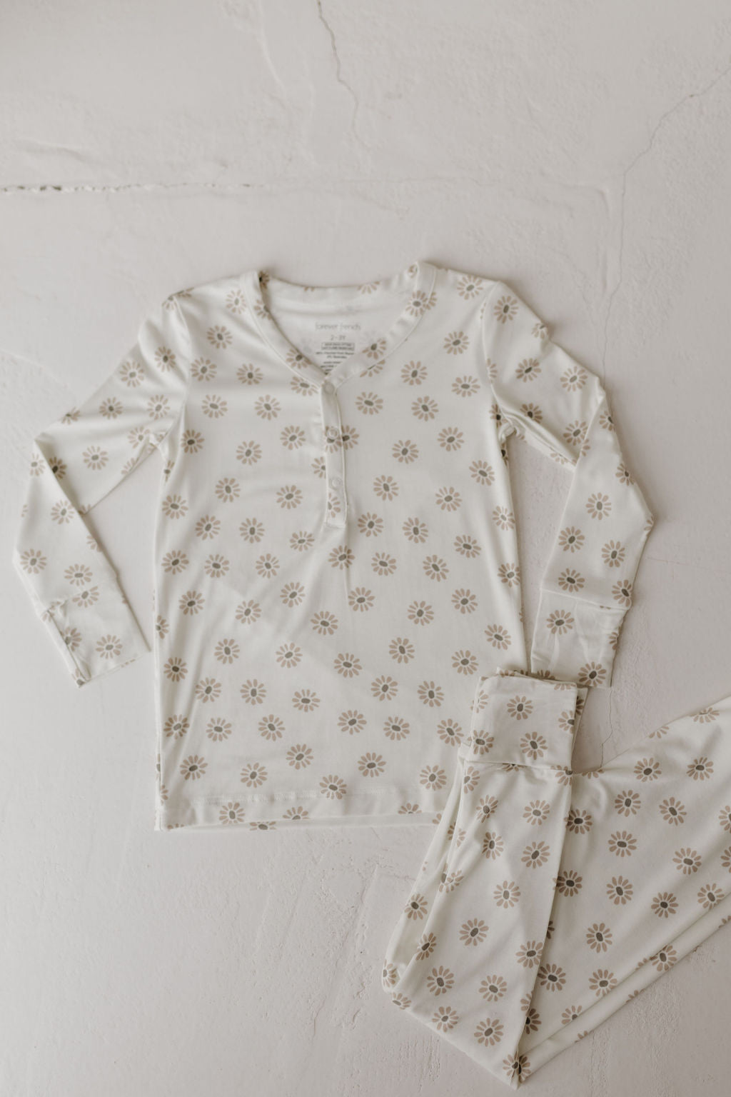 The "Bamboo Two Piece Pajamas | Daisy Fields" by forever french baby is a white long-sleeve set with a buttoned collar, laid flat on a light surface. Made from breathable fabric, these pajamas feature small muted floral designs for ultimate comfort and elegance.