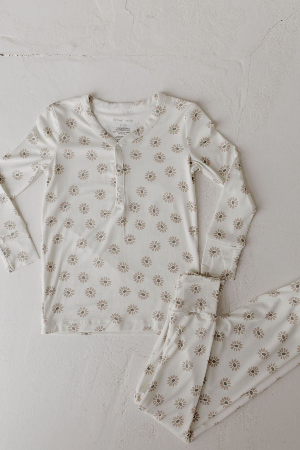 The Daisy Fields Bamboo Two Piece Pajamas by forever french baby features a floral pattern with a breathable, white bamboo long-sleeved button-up top and matching pants, showcased on a light textured surface.