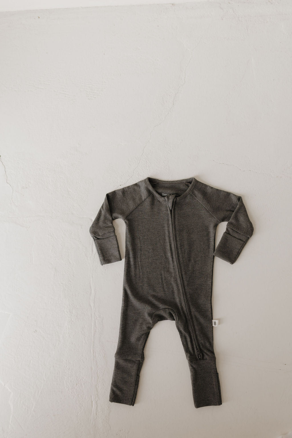 The Bamboo Zip Pajamas in Shadow from forever french baby, made of hypoallergenic bamboo fabric, feature a charcoal gray long-sleeve design. It offers comfort and easy wear with its soft ribbed material and front zipper, laid flat on a light-textured surface for display.