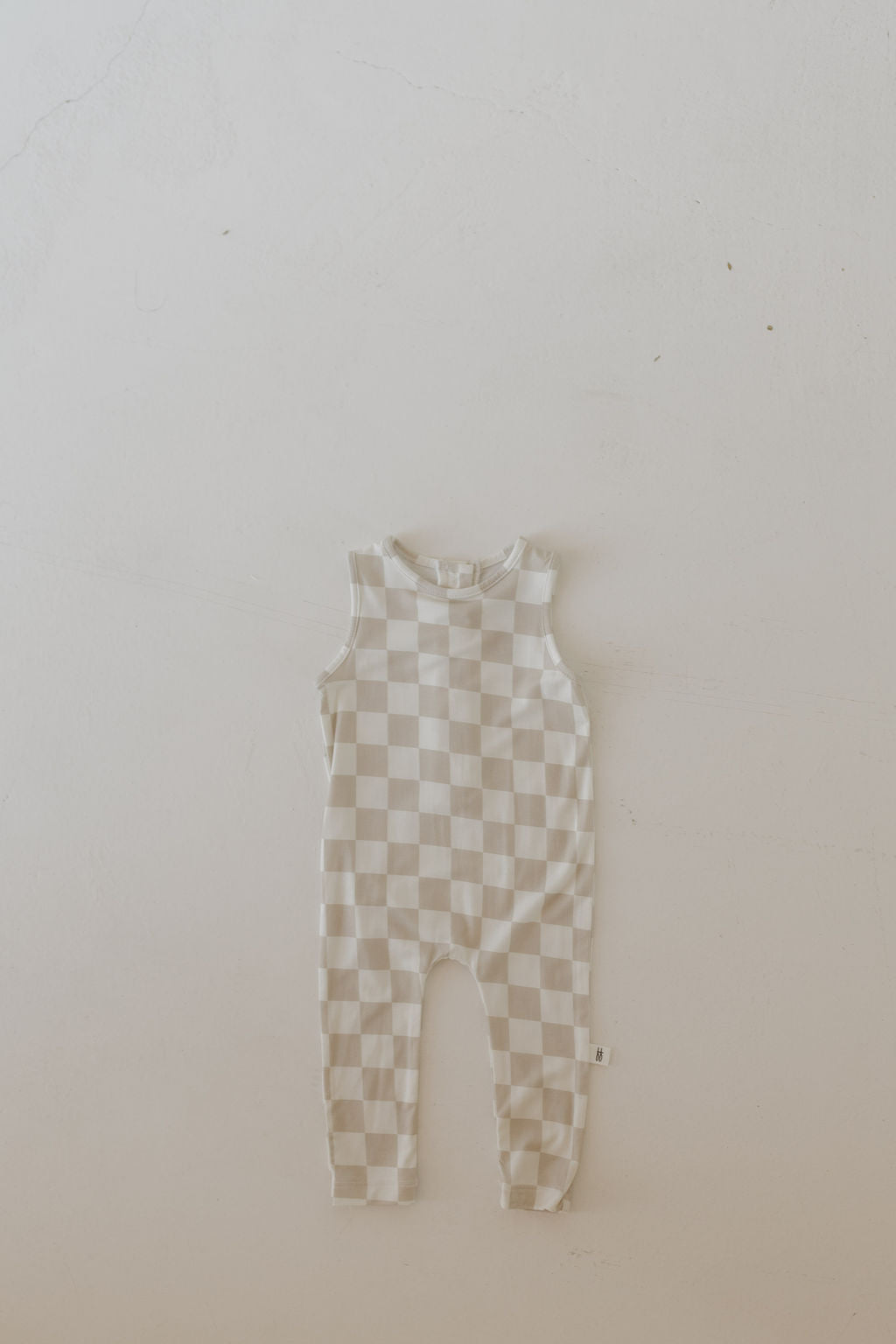 A beige and off-white checkered Harem Bamboo Romper by forever french baby is laid flat on a plain, light-colored surface.