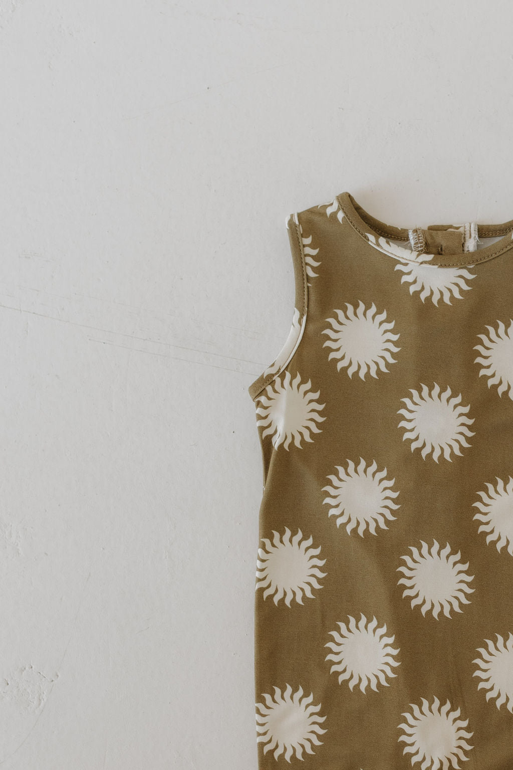 The Harem Bamboo Romper | Sol by forever french baby is partially displayed on a light neutral surface, showcasing its airy elegance with a beige background and white sun patterns in breathable bamboo fabric.