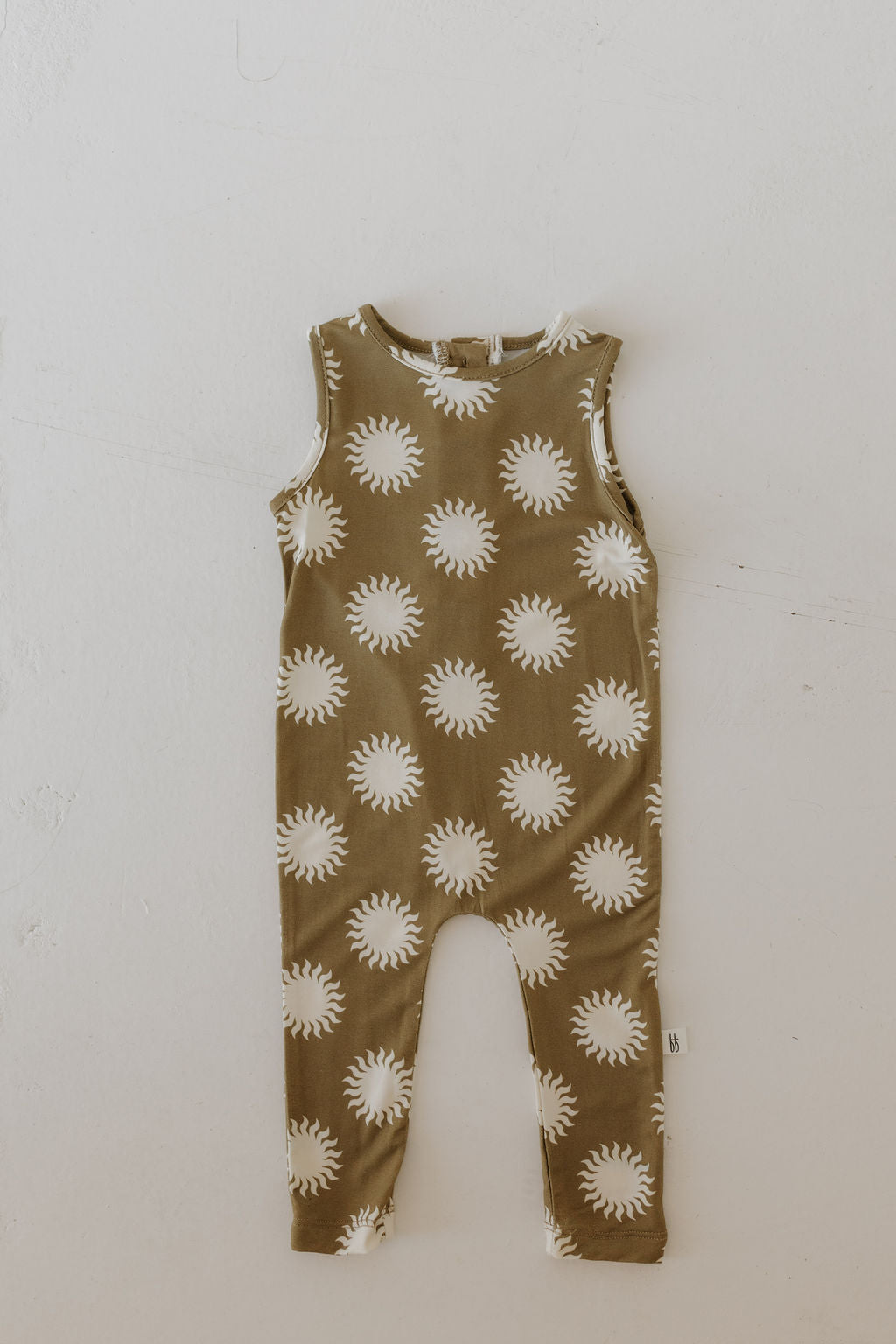 The Harem Bamboo Romper | Sol by forever french baby is an olive-green, sleeveless romper with white sunburst patterns, made from breathable bamboo fabric. It features a simple design with a round neckline and long legs, displayed on a light neutral background.