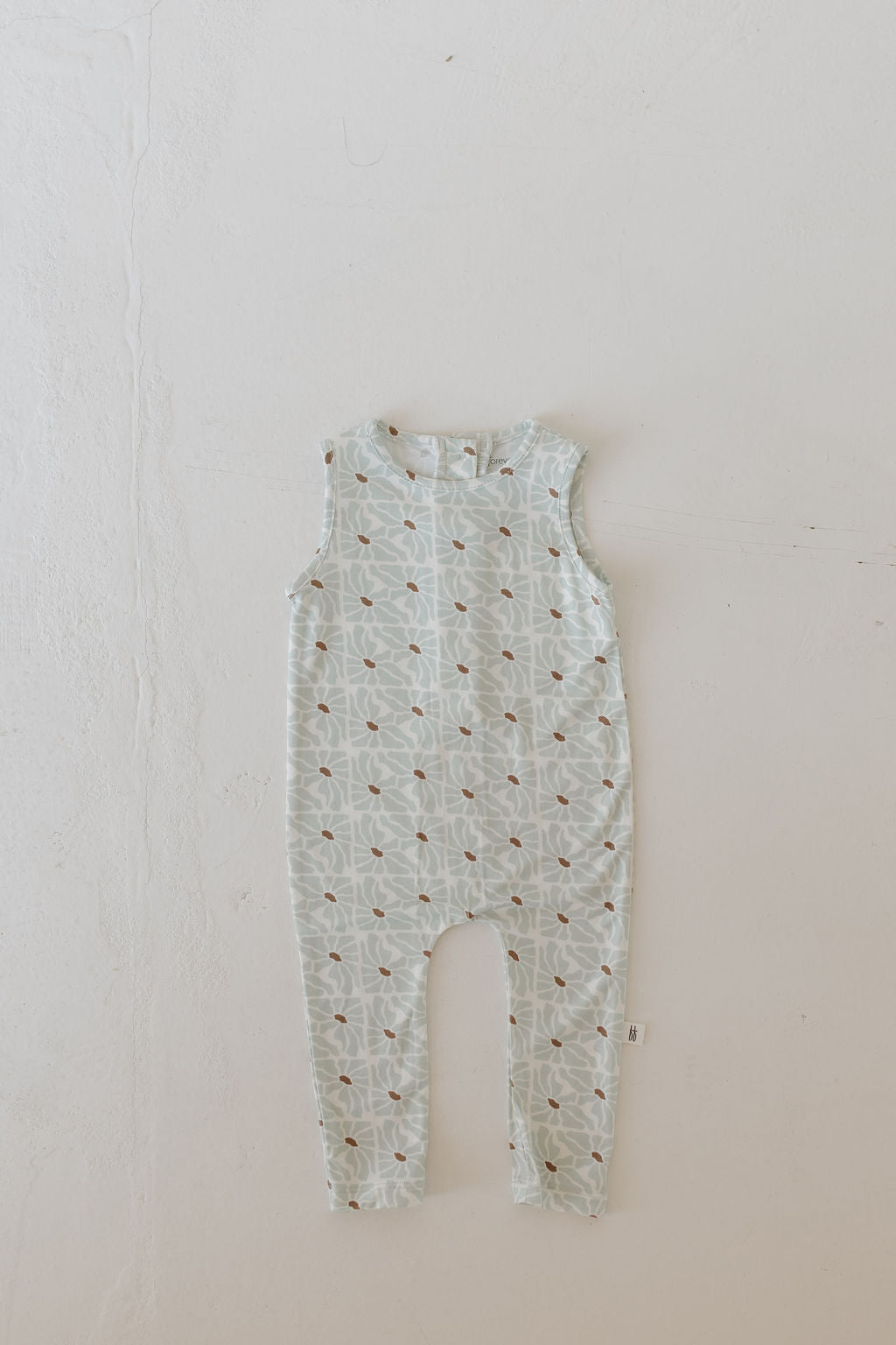 The "Harem Bamboo Romper | Coast" by forever french baby is a sleeveless romper with a flower geometric pattern on light teal, laid flat on white. Made from breathable fabric, it's designed for added comfort.