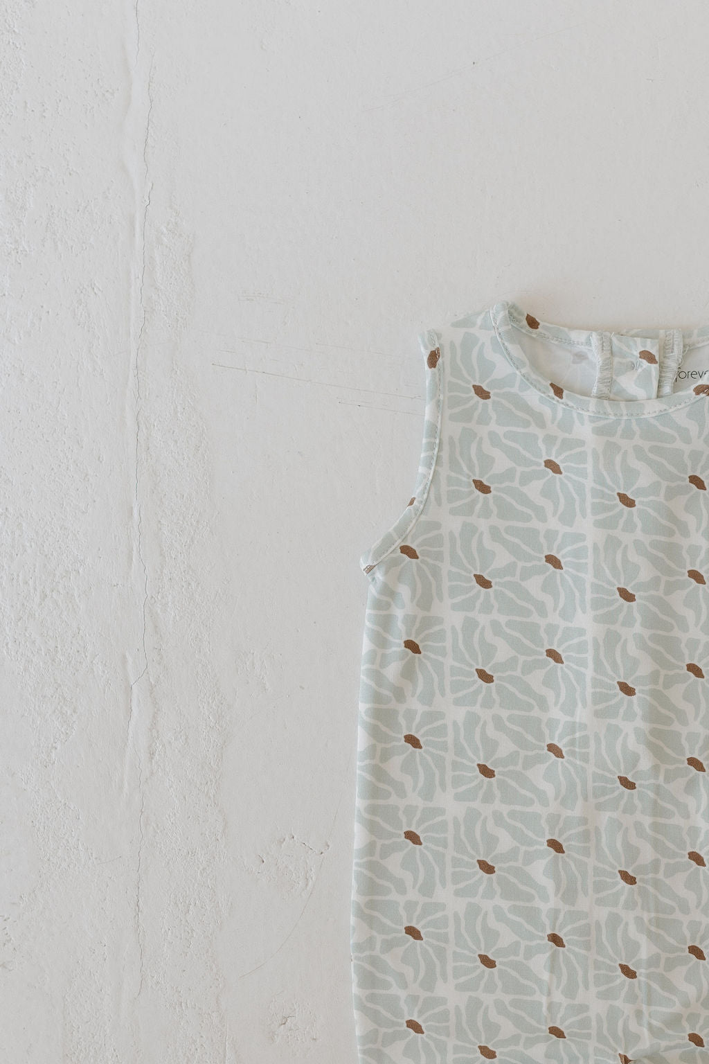 The Harem Bamboo Romper by forever french baby combines style and comfort with its breathable fabric, featuring a light blue and white floral pattern accented by small brown dots. Laid flat on an off-white surface, this sleeveless romper is perfect for any occasion.