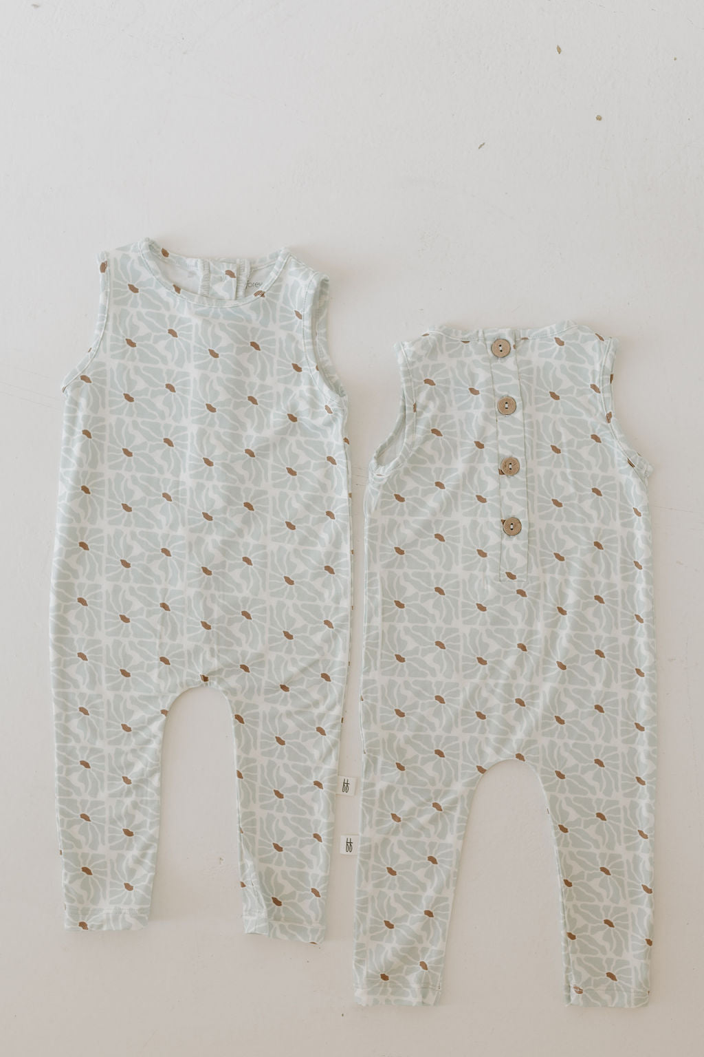 Two Harem Bamboo Rompers by forever french baby are laid flat, crafted in breathable, hypo-allergenic light blue fabric. They feature a brown floral pattern, and the front and back views show buttons on one for easy wear.