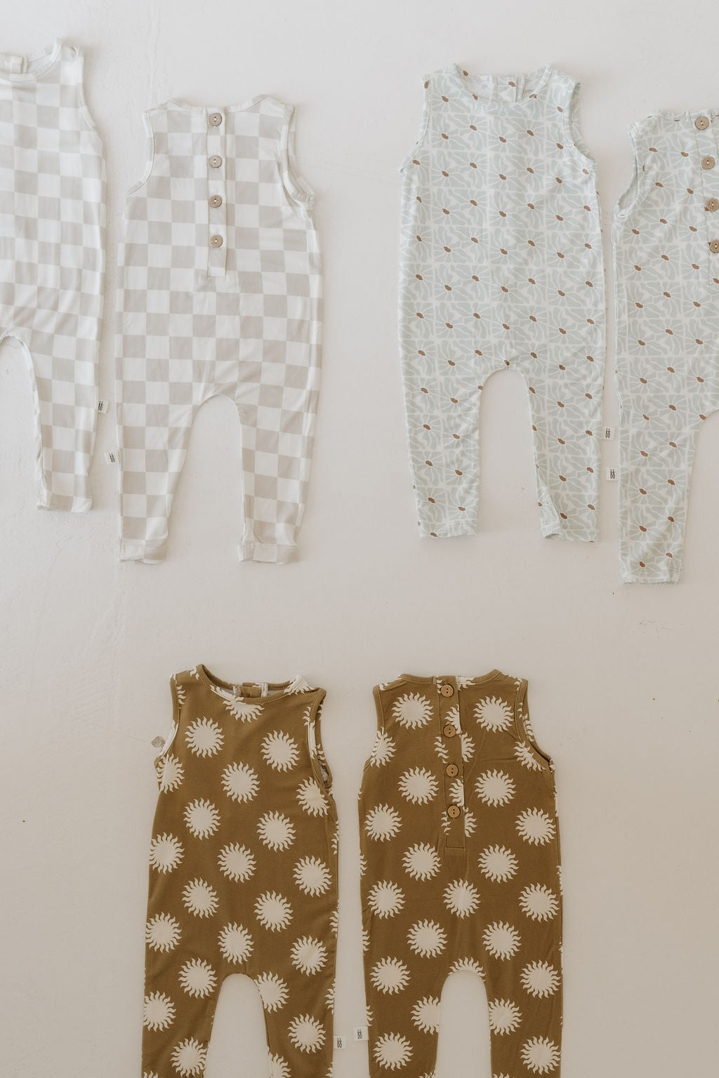 Four Harem Bamboo Rompers by forever french baby, crafted from hypo-allergenic bamboo fabric, are displayed on a white background. The top row features checkered and patterned designs, while the bottom row shows charming daisy patterns. All rompers are sleeveless and styled for infant comfort.