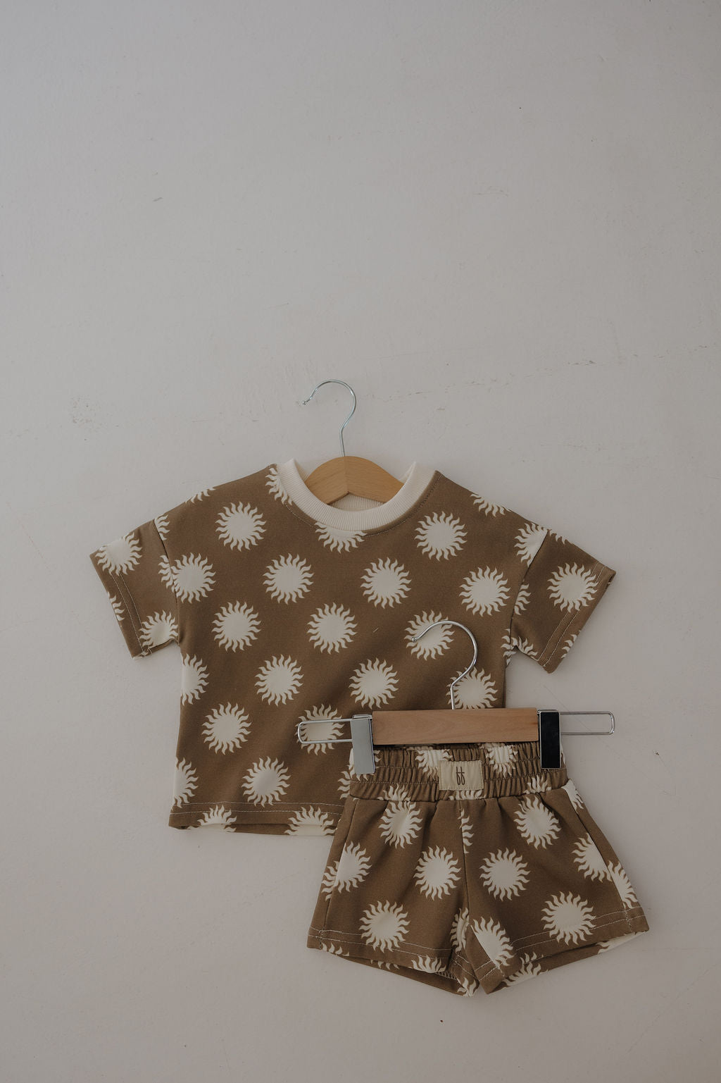 The French Terry Short Set | Sol by forever french baby is a two-piece kids’ outfit with a soft cotton blend, featuring a short-sleeve brown shirt and matching shorts adorned with a white sun pattern.