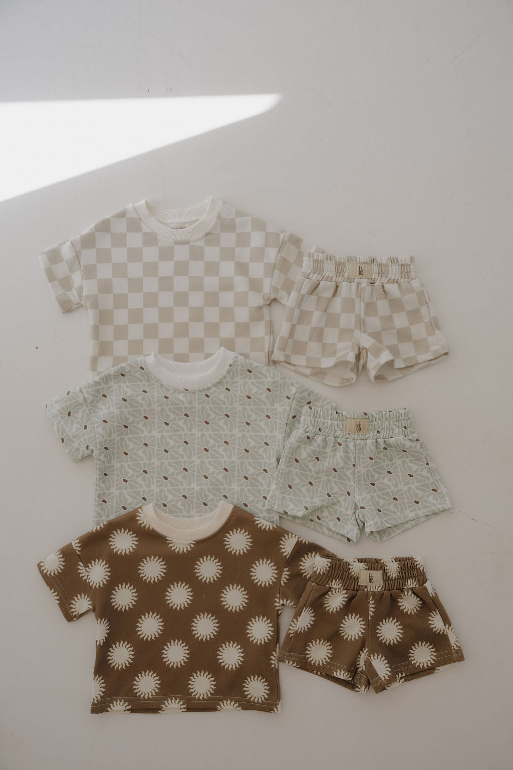 Three French Terry Short Sets by forever french baby are displayed: beige and white checkered, mint with small brown dots, and brown with white sun patterns on a light background.