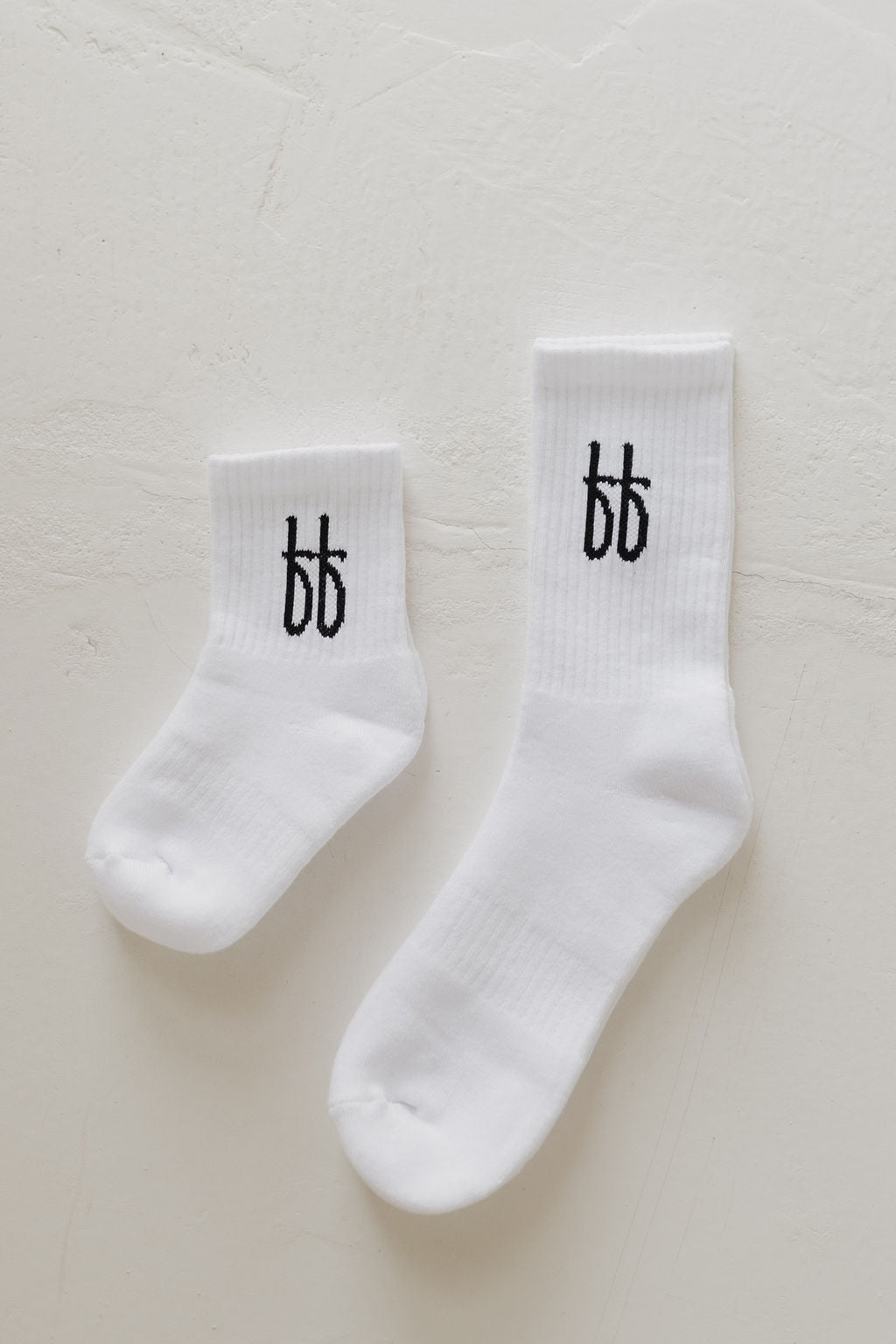 A comfy pair of white ff Crew Socks, by forever french baby, each featuring the black "bb" logo on the ankle and one slightly smaller than the other, displayed on a light textured surface—ideal for everyday wear.