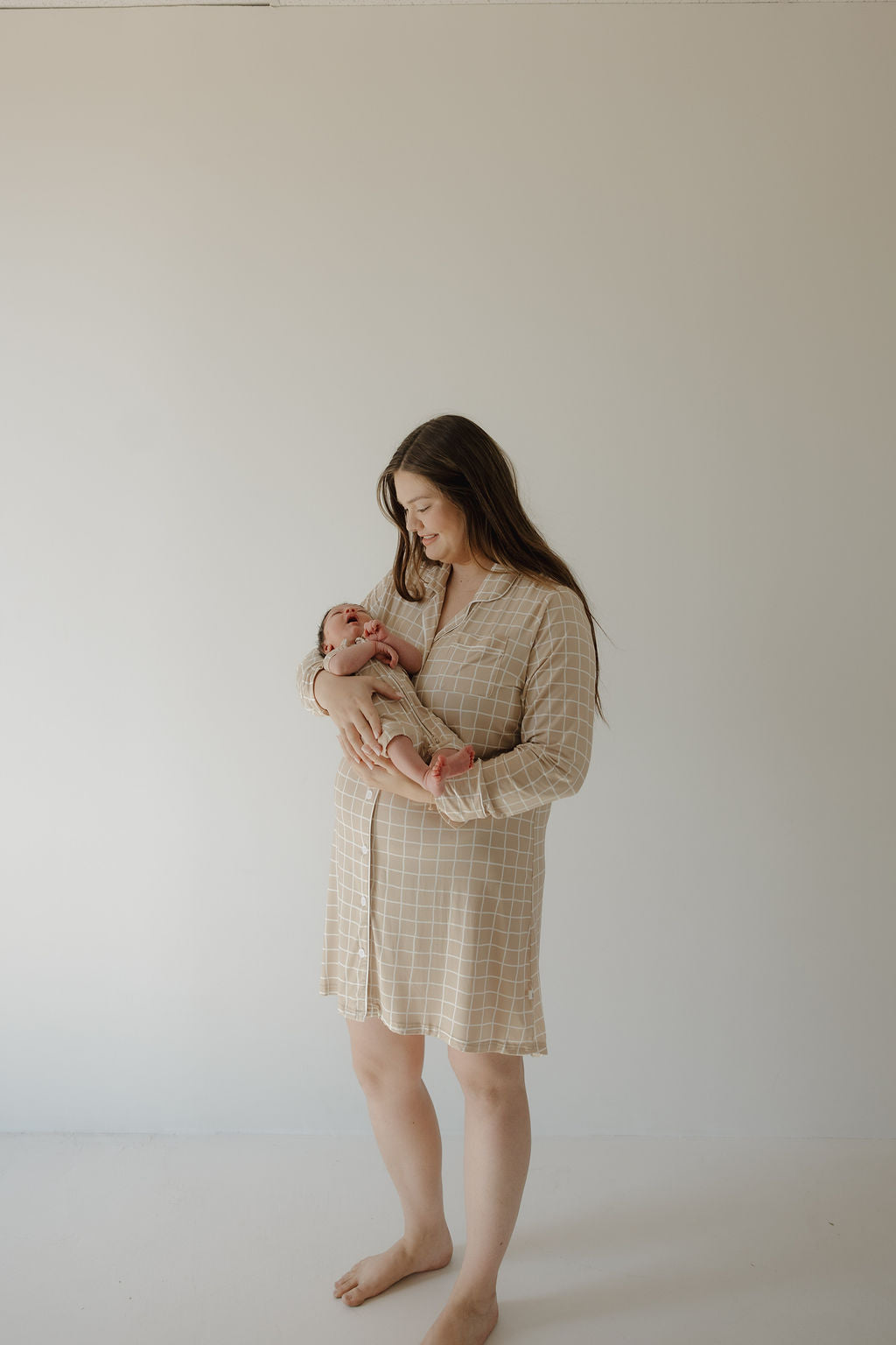 A barefoot woman smiles as she cradles a newborn, wearing the forever french baby Women's Bamboo Sleeping Dress | Grid against a plain light background.
