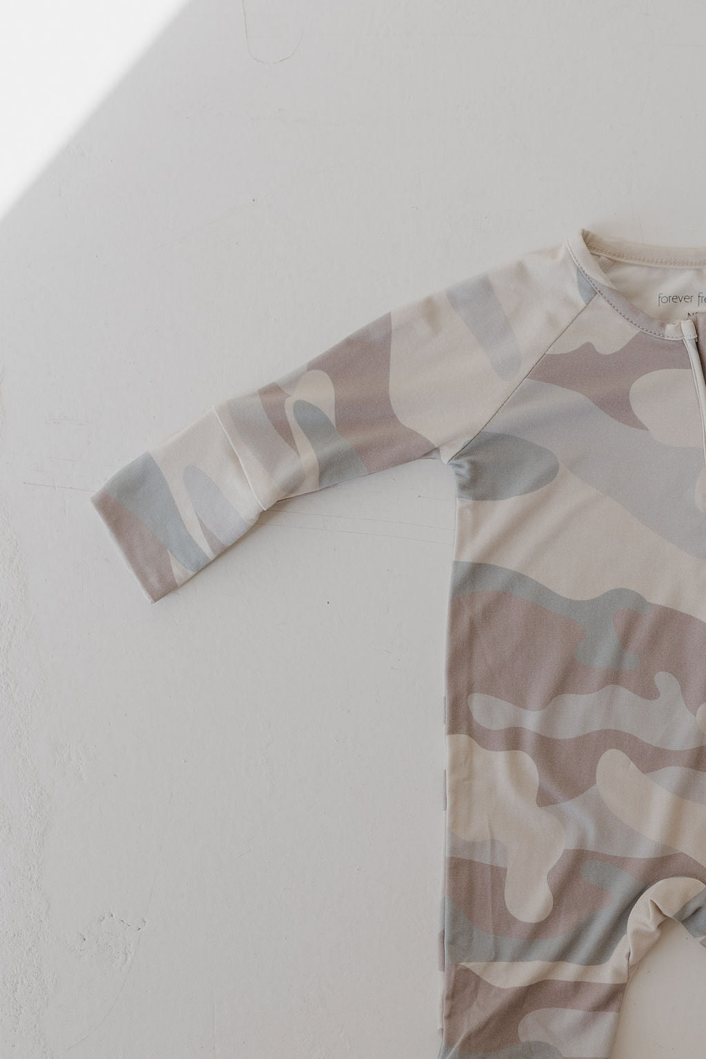 The forever french baby Bamboo Zip Pajamas feature a cozy long-sleeve romper with a beige, gray, and light brown camouflage pattern on a light backdrop. Made from breathable sleepwear fabric, the image emphasizes its unique texture and upper design.