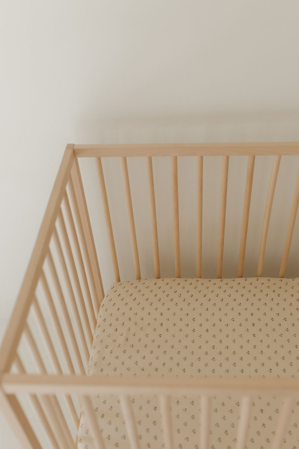 A Muslin Crib Sheet | Flora by forever french baby covers a wooden baby crib, featuring a light brown, patterned mattress set against a plain, light-colored backdrop.
