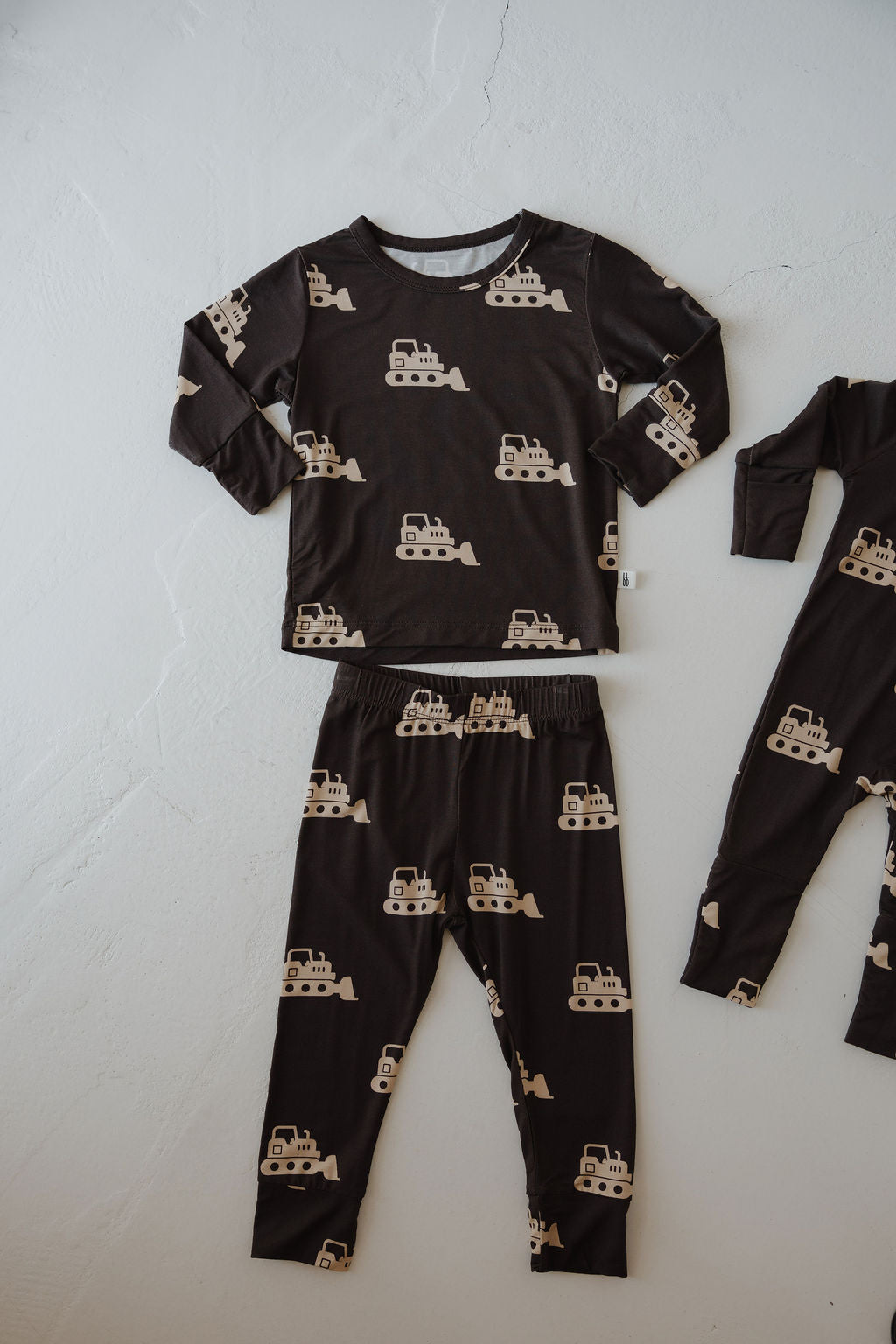 The forever french baby Child Sleepy Time Set | Bulldozer features dark, breathable long-sleeve pajamas with beige bulldozer patterns, shown on a light textured surface.