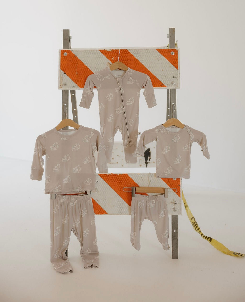 Four light beige bamboo Sleepy Time Set | Excavator pieces by forever french baby, featuring white animal prints, hang on wooden hangers before an orange-and-white barricade—an ideal breathable lounge set for babies and toddlers.