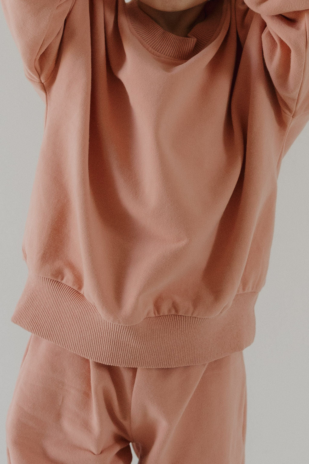 A child is shown from shoulders to thighs wearing the forever french baby Child Sweat Set in Rose, arms raised and ready for everyday adventures, set against a plain background.