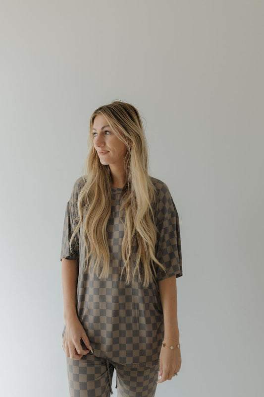 A person with long blonde hair poses against a plain background, wearing an oversized Short Sleeve Women's Bamboo Pajama in Faded Checkerboard by forever french baby. The hypo-allergenic set's relaxed fit complements their serene gaze to the side.