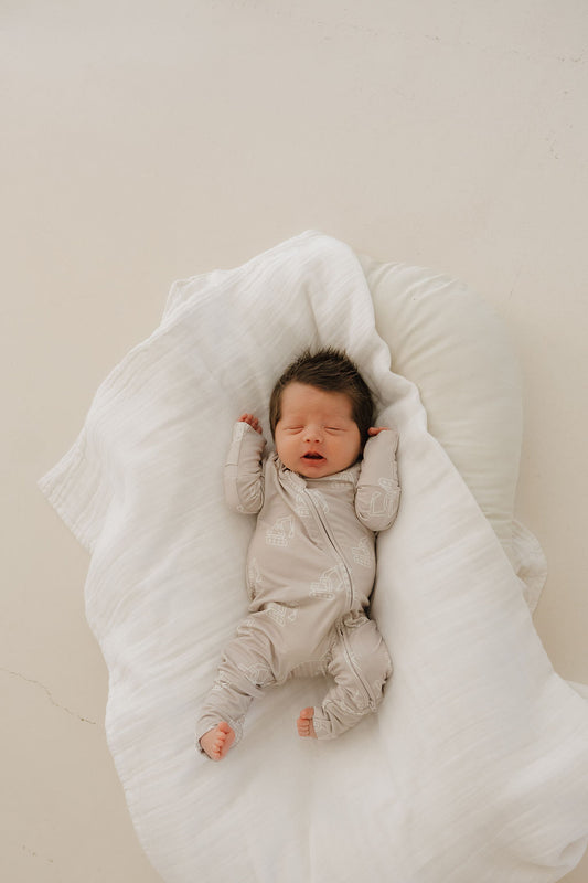 A newborn with dark hair sleeps on a white blanket, wearing forever french baby's Bamboo Zip Pajamas | Excavator—hypo-allergenic and made from premium bamboo, featuring subtle patterns.