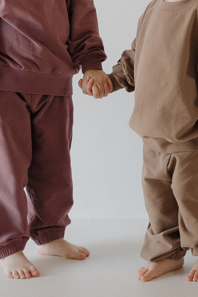Two young children wear matching forever french baby Child Sweat Set in Twilight, standing barefoot and holding hands on a light floor—showcasing a coordinated family look with their heads out of frame.