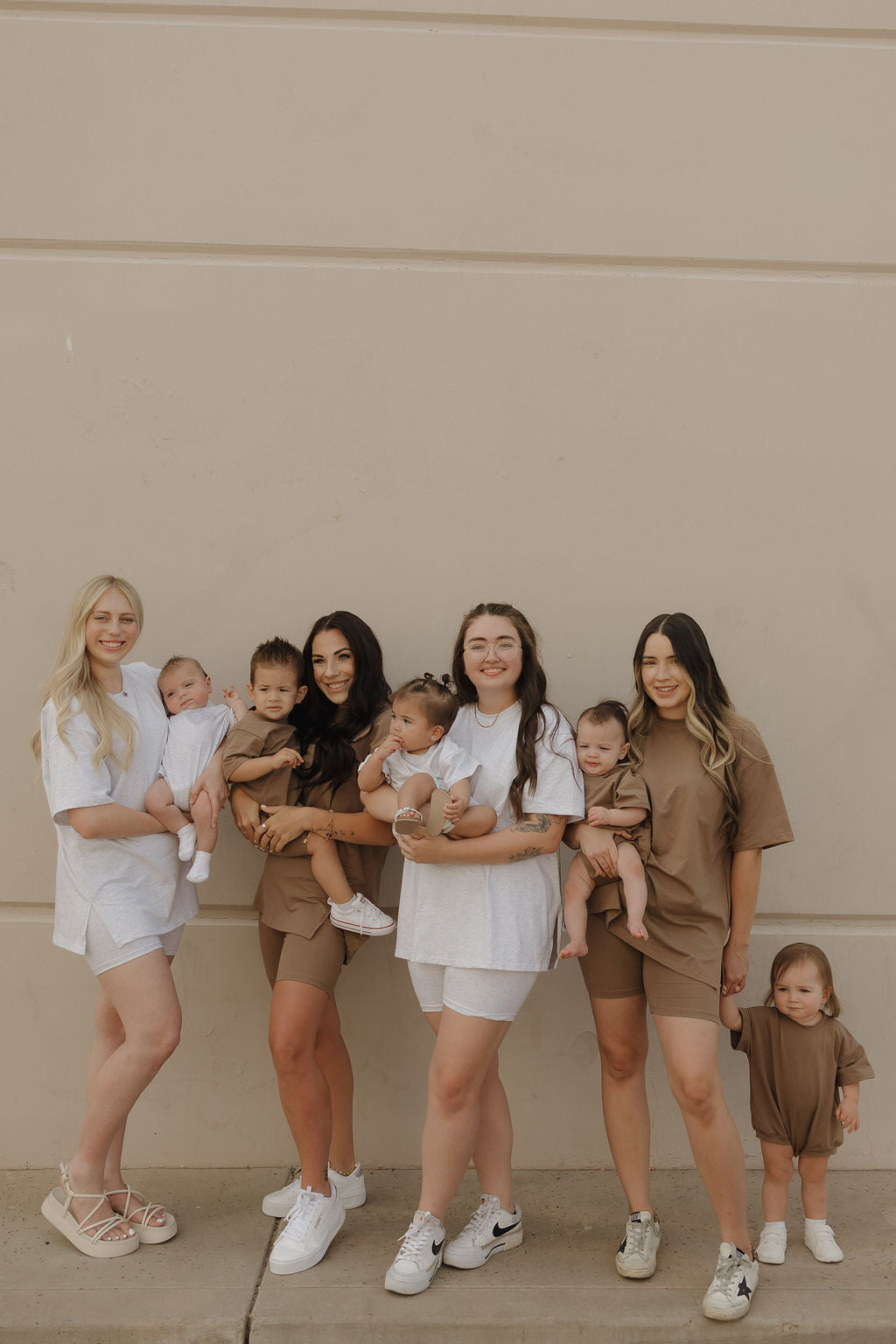 Four women in forever french baby Women's Short Set | Patina smile with five young children, all dressed in coordinating colors, standing together in front of a beige wall.