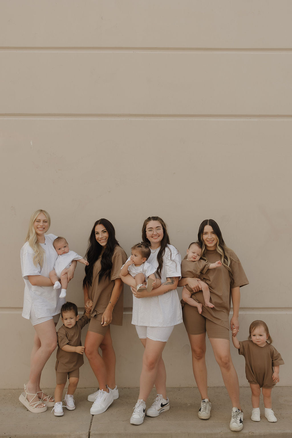Four women stand together holding babies, with two toddlers in front. All are dressed casually in neutral tones, and the little ones wear comfy forever french baby Short Sleeve Romper | Patina.