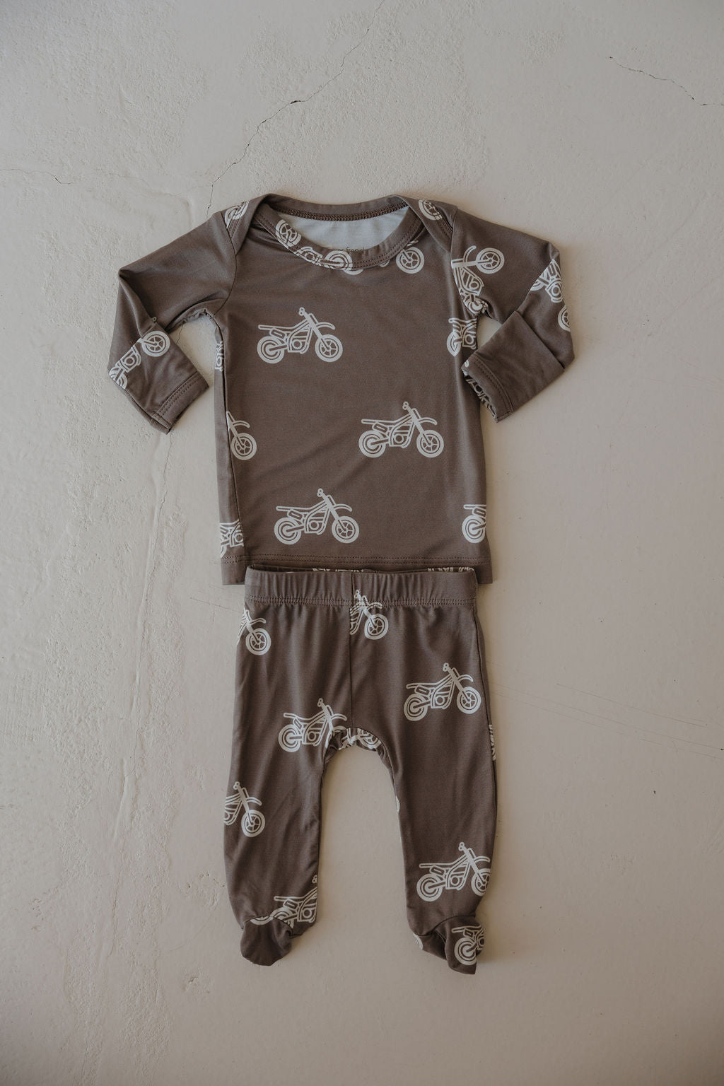 The Sleepy Time Set | Dirt Bike by forever french baby features a brown long-sleeve top and matching pants with white motorcycle prints, laid flat on a light textured surface. This hypo-allergenic set is perfect for cozy nights.