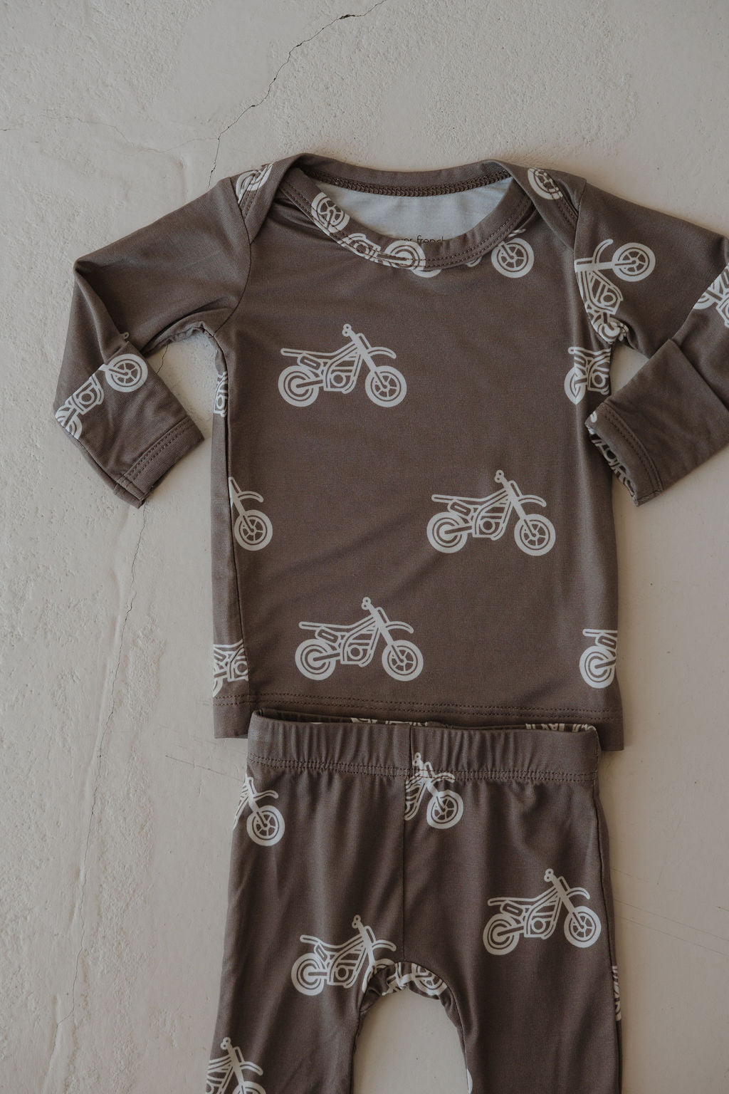 The forever french baby Sleepy Time Set | Dirt Bike is a hypoallergenic, brown long-sleeve children’s set with white motorcycle prints, shown laid flat on a light background.