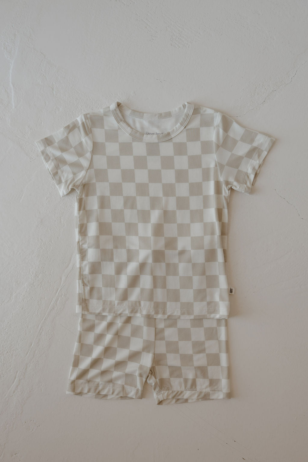 The forever french baby Bamboo Short Set | Checkerboard features a beige and white checkerboard pattern in breathable bamboo, displayed flat on a textured white surface.