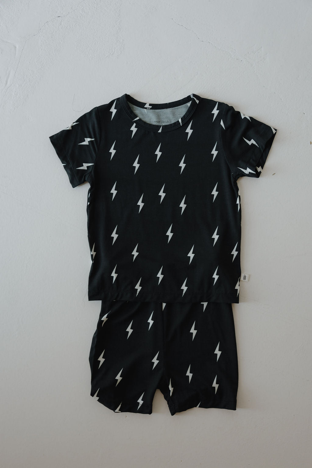 The Bamboo Short Set | Midnight Lightning Bolt by forever french baby features a black, short-sleeve shirt and shorts with a white lightning bolt pattern, made from soft bamboo fabric, displayed flat on a light background.